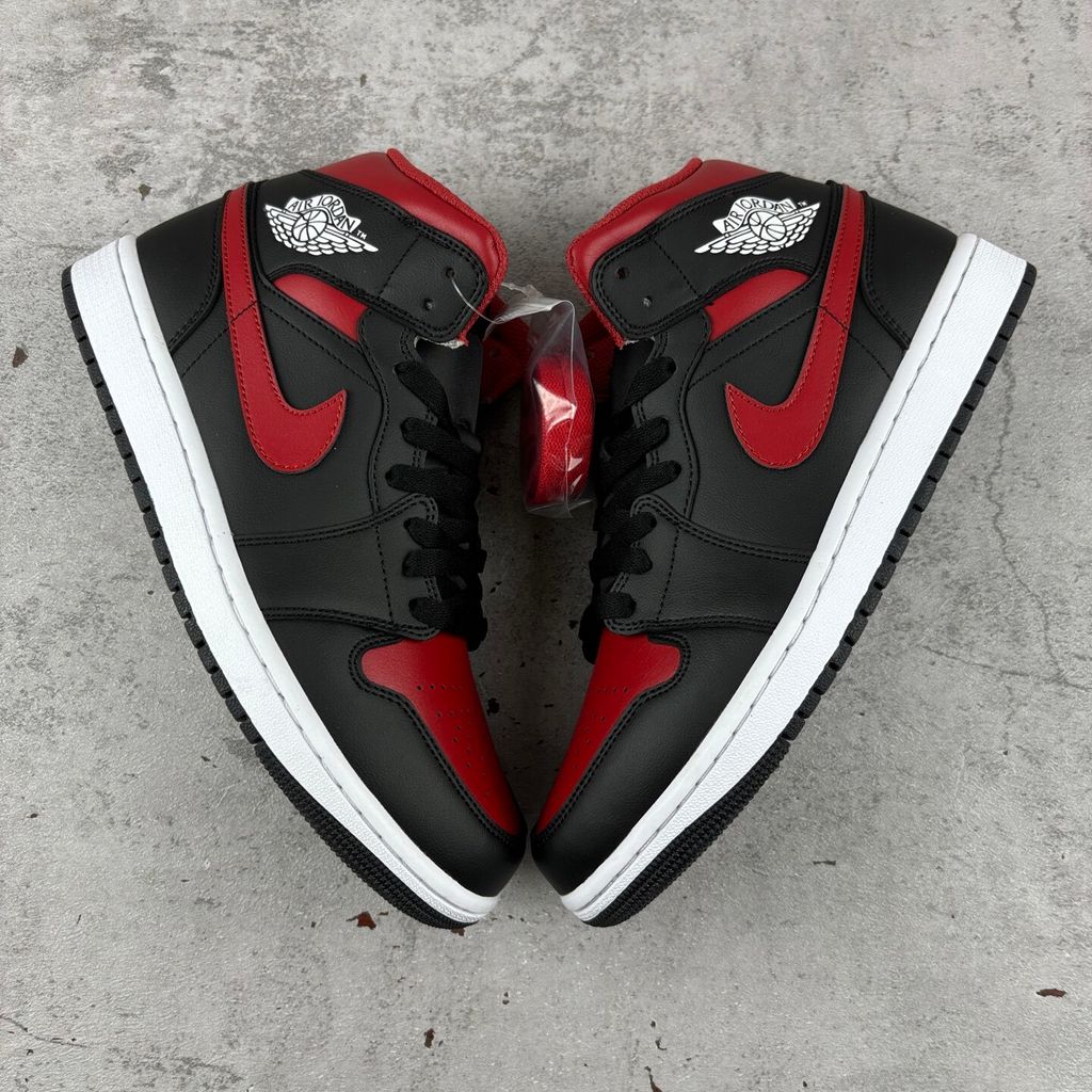 Side profile of the Air Jordan 1 Mid sneaker in the 'Bred Twist' colorway, featuring a crisp white leather base, bold black overlays, and vibrant University Red accents on the Swoosh, collar, and outsole.