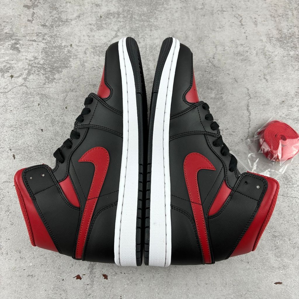 Side profile of the Air Jordan 1 Mid sneaker in the 'Bred Twist' colorway, featuring a crisp white leather base, bold black overlays, and vibrant University Red accents on the Swoosh, collar, and outsole.