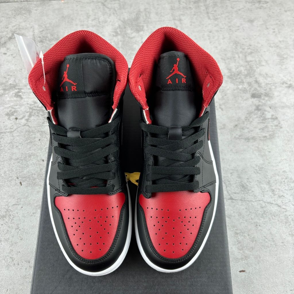 Side profile of the Air Jordan 1 Mid sneaker in the 'Bred Twist' colorway, featuring a crisp white leather base, bold black overlays, and vibrant University Red accents on the Swoosh, collar, and outsole.