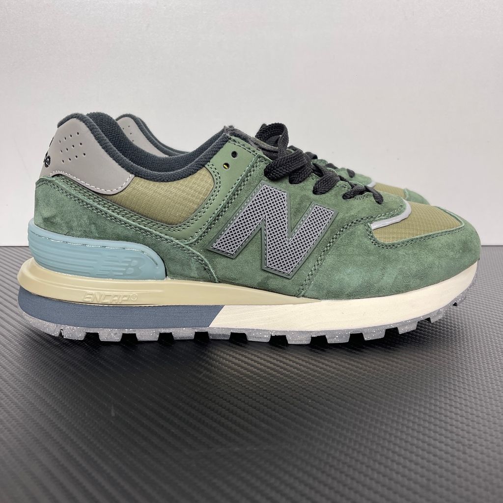 Side profile of the New Balance 574 Legacy Stone Island sneaker featuring a tactical dark green ripstop and suede upper, the iconic Stone Island compass logo on the tongue, and a rugged grey ENCAP midsole.