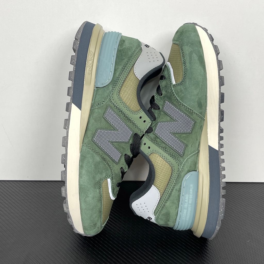 Side profile of the New Balance 574 Legacy Stone Island sneaker featuring a tactical dark green ripstop and suede upper, the iconic Stone Island compass logo on the tongue, and a rugged grey ENCAP midsole.