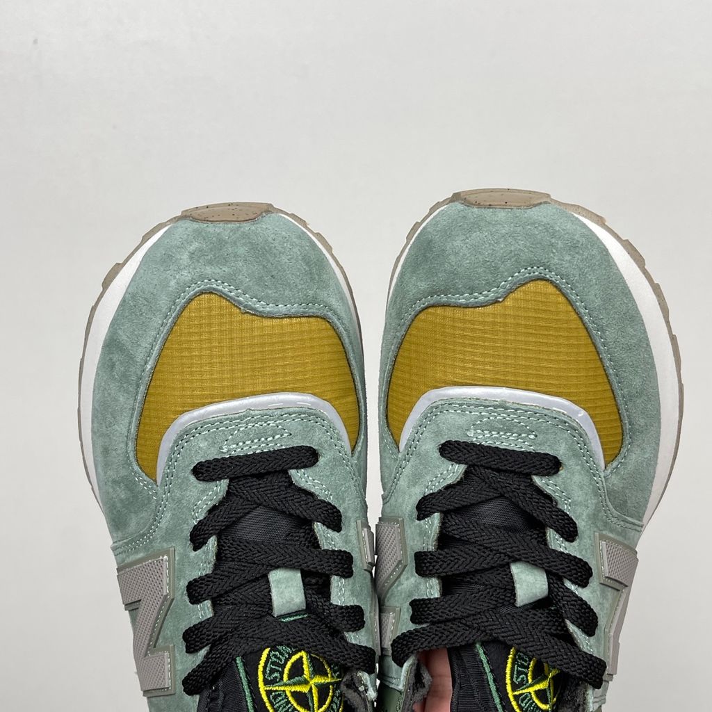 Side profile of the New Balance 574 Legacy Stone Island sneaker featuring a tactical light green ripstop and suede upper, the iconic Stone Island compass logo on the tongue, and a rugged grey ENCAP midsole.