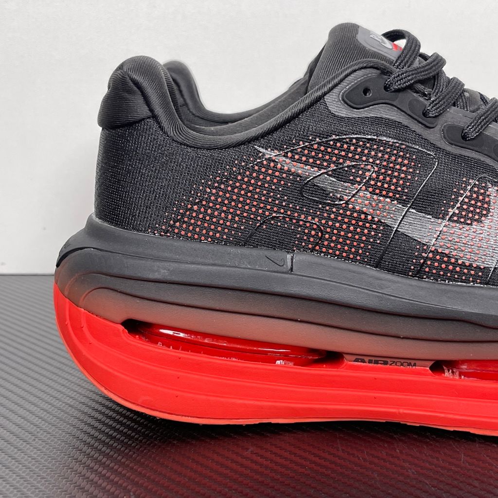 Side profile of the Nike Vomero Premium sneaker featuring a stealthy black mesh upper with oversized 'AIR' branding, and a massive gradient platform midsole transitioning from black to bright crimson with exposed Zoom Air units.