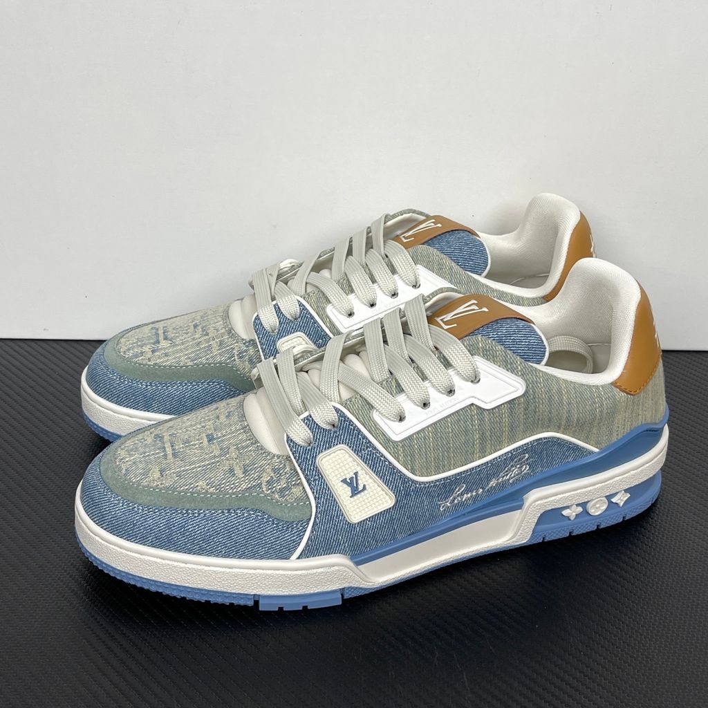 Side profile of the Tyler, the Creator x Louis Vuitton LV Trainer sneaker, showcasing a mix of light grey and blue denim paneling, a contrasting brown leather heel tab, the LV Initials logo, and custom cursive Louis Vuitton embroidery on the lateral side.