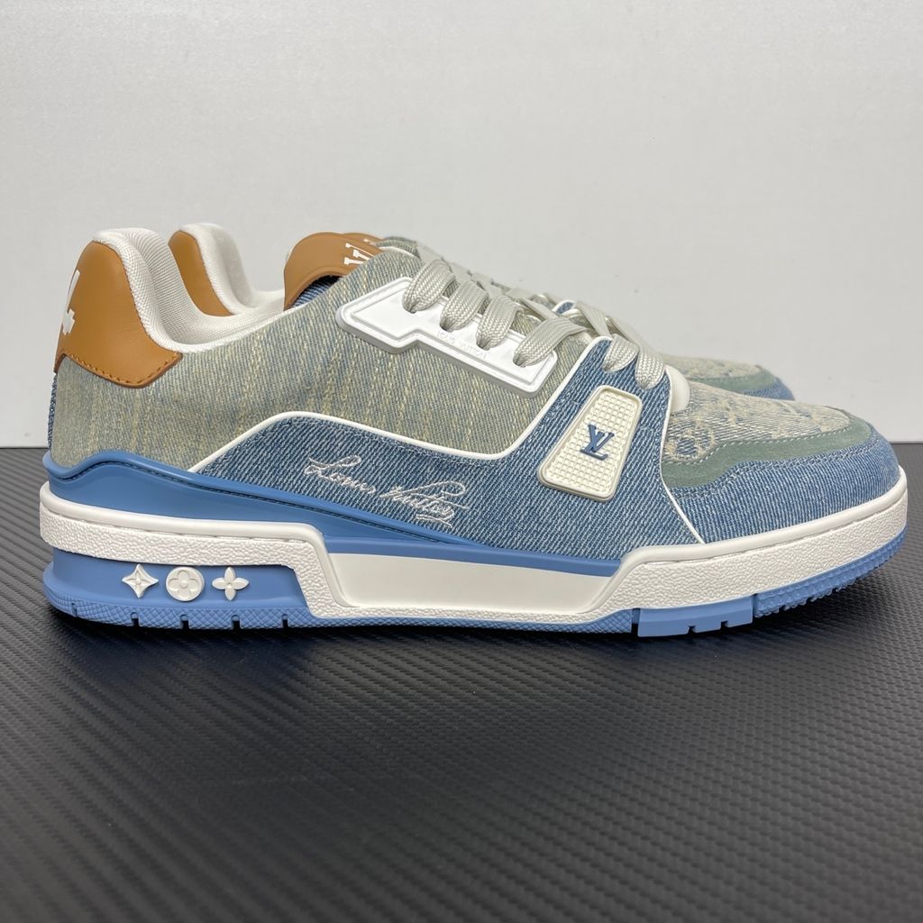 Side profile of the Tyler, the Creator x Louis Vuitton LV Trainer sneaker, showcasing a mix of light grey and blue denim paneling, a contrasting brown leather heel tab, the LV Initials logo, and custom cursive Louis Vuitton embroidery on the lateral side.