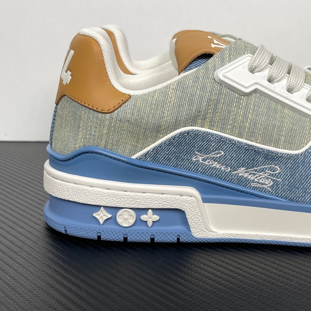 Side profile of the Tyler, the Creator x Louis Vuitton LV Trainer sneaker, showcasing a mix of light grey and blue denim paneling, a contrasting brown leather heel tab, the LV Initials logo, and custom cursive Louis Vuitton embroidery on the lateral side.
