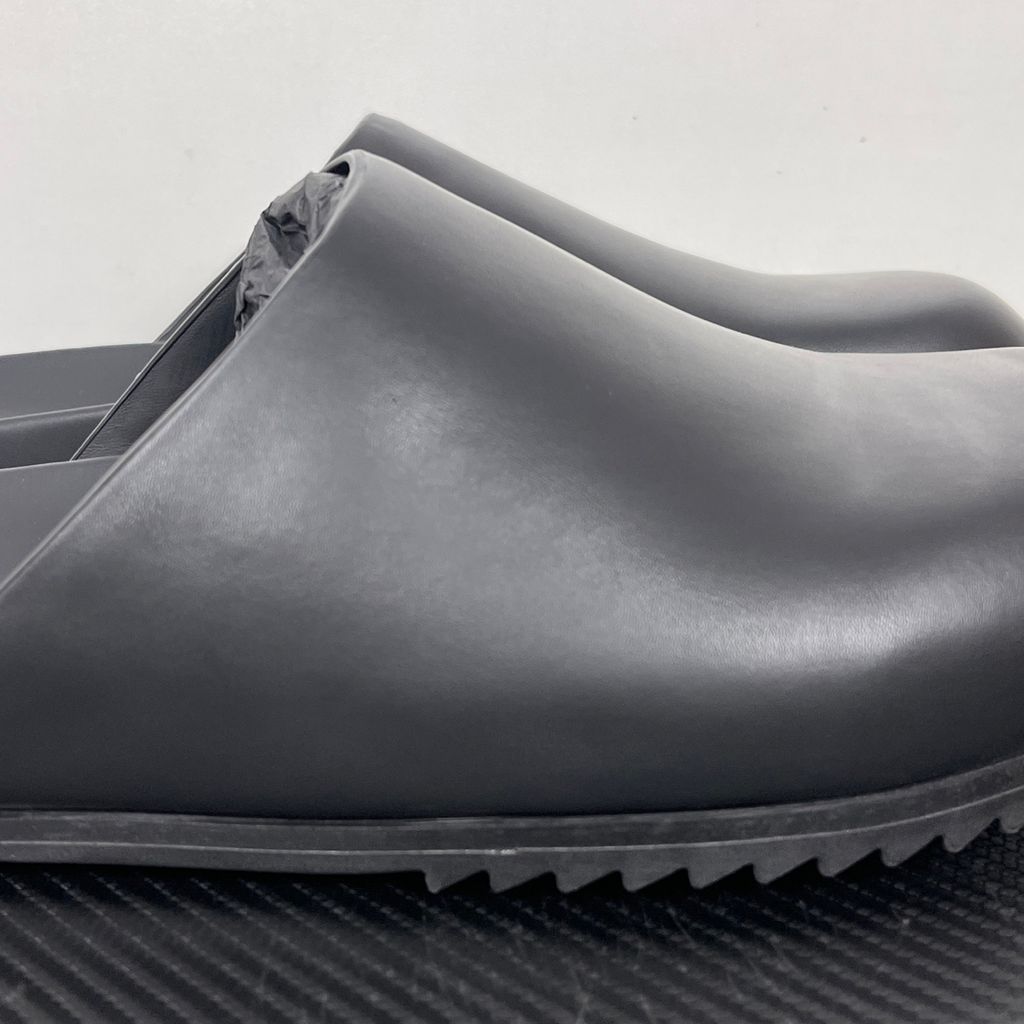 Side profile of the Rick Owens Mule Granola in smooth black leather, featuring a minimalist slip-on silhouette, an exaggerated rounded toe box, and a signature dark jagged rubber outsole.