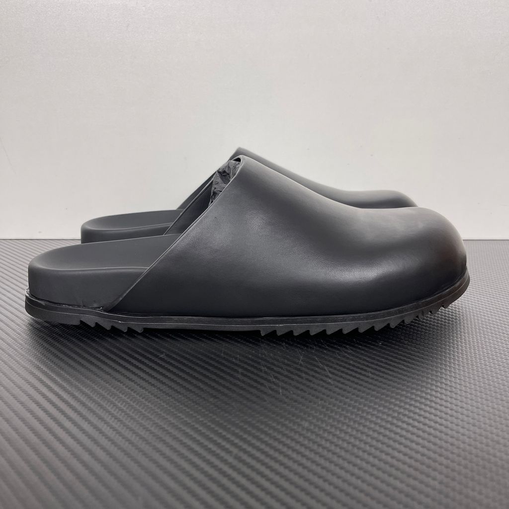 Side profile of the Rick Owens Mule Granola in smooth black leather, featuring a minimalist slip-on silhouette, an exaggerated rounded toe box, and a signature dark jagged rubber outsole.