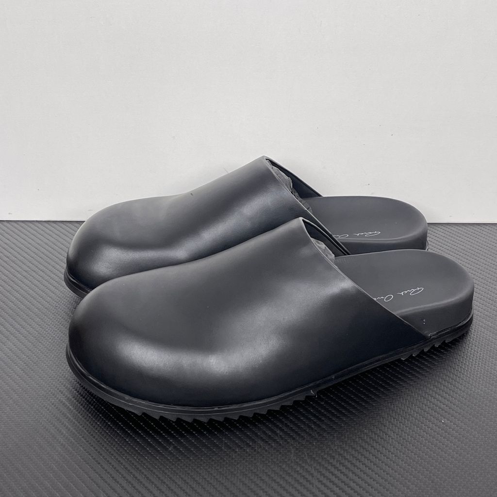Side profile of the Rick Owens Mule Granola in smooth black leather, featuring a minimalist slip-on silhouette, an exaggerated rounded toe box, and a signature dark jagged rubber outsole.