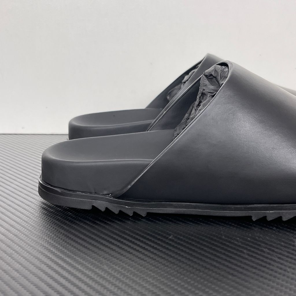 Side profile of the Rick Owens Mule Granola in smooth black leather, featuring a minimalist slip-on silhouette, an exaggerated rounded toe box, and a signature dark jagged rubber outsole.