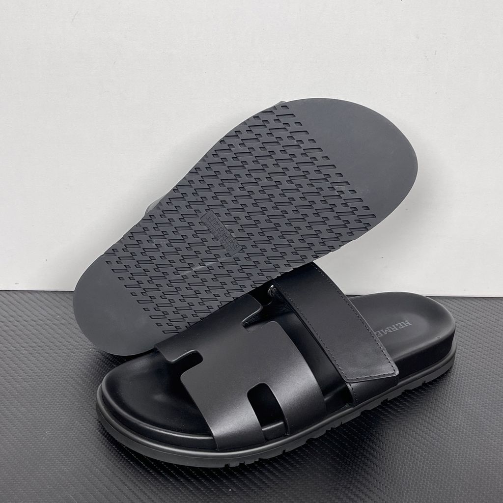 Side profile of the Hermès Chypre sandal crafted in smooth black calfskin leather, featuring the signature 'H' cut-out design across the toe, an adjustable velcro strap over the instep, and a contoured anatomical rubber sole.