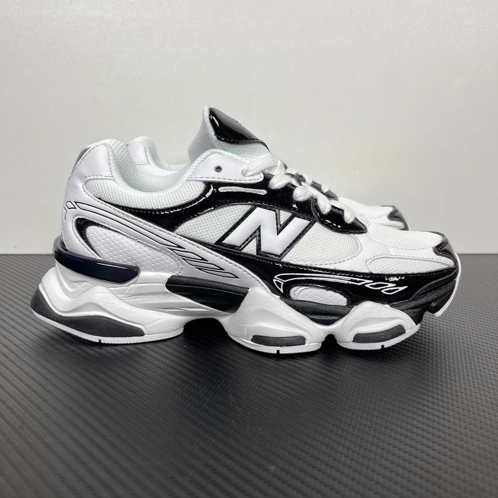 Side profile of the New Balance 9060 sneaker in a sleek black and white colorway, featuring a complex mixed-material upper of suede and mesh, a prominent contrasting 'N' logo, and a highly sculpted chunky midsole with distinctive pod detailing.