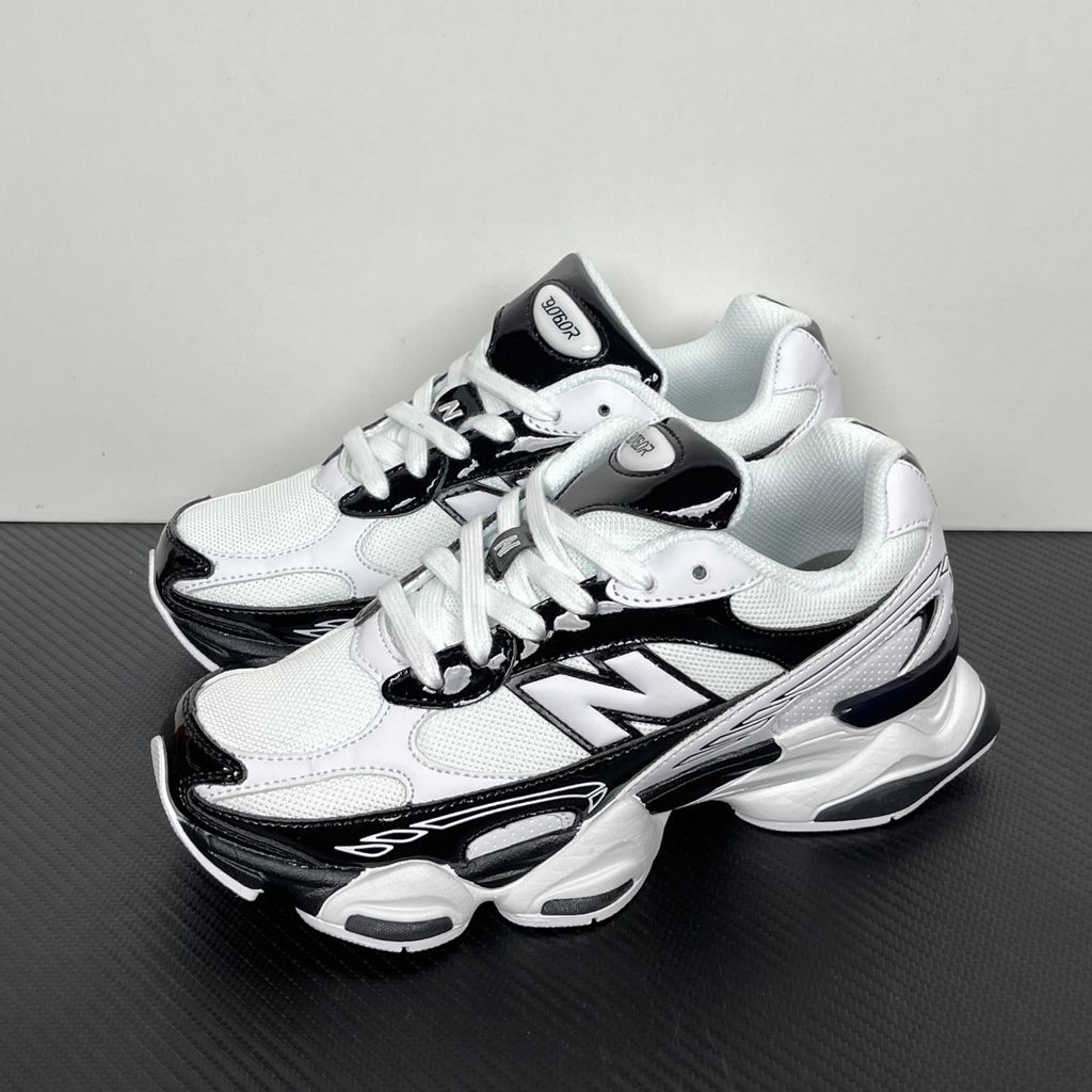 Side profile of the New Balance 9060 sneaker in a sleek black and white colorway, featuring a complex mixed-material upper of suede and mesh, a prominent contrasting 'N' logo, and a highly sculpted chunky midsole with distinctive pod detailing.