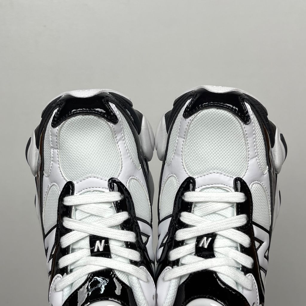 Side profile of the New Balance 9060 sneaker in a sleek black and white colorway, featuring a complex mixed-material upper of suede and mesh, a prominent contrasting 'N' logo, and a highly sculpted chunky midsole with distinctive pod detailing.