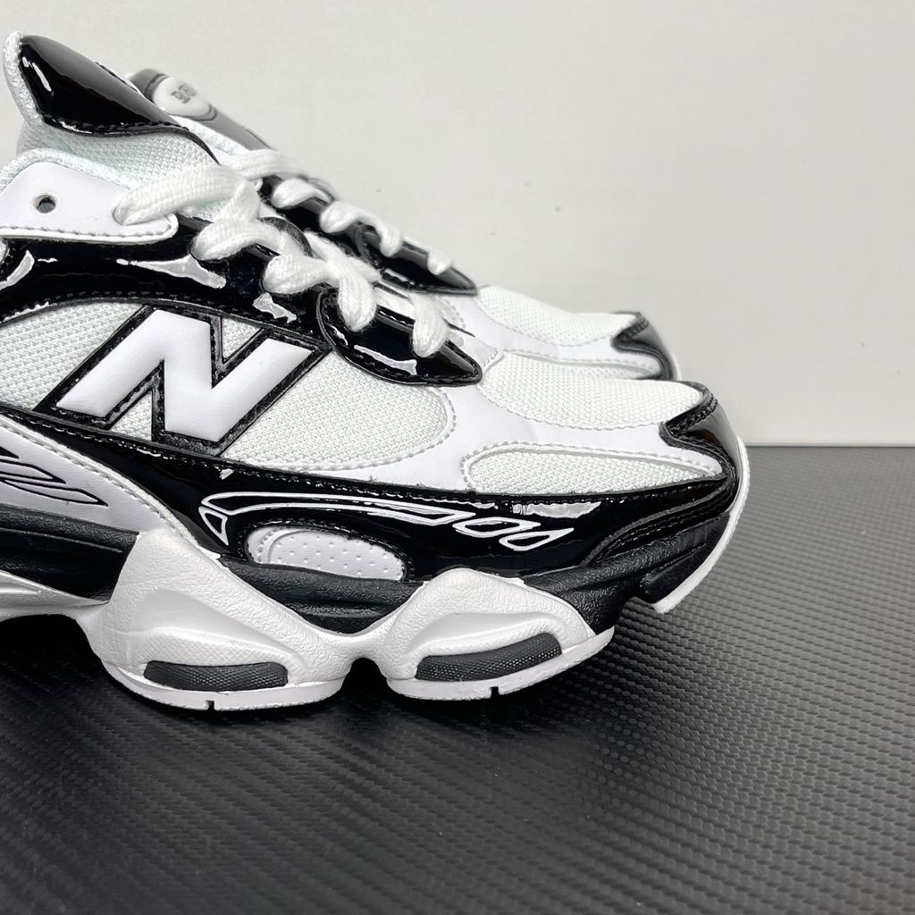 Side profile of the New Balance 9060 sneaker in a sleek black and white colorway, featuring a complex mixed-material upper of suede and mesh, a prominent contrasting 'N' logo, and a highly sculpted chunky midsole with distinctive pod detailing.