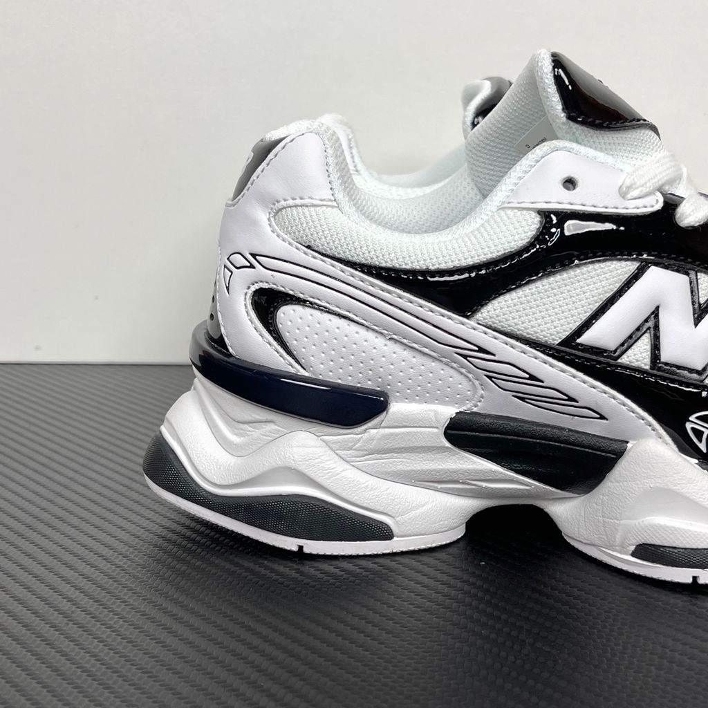 Side profile of the New Balance 9060 sneaker in a sleek black and white colorway, featuring a complex mixed-material upper of suede and mesh, a prominent contrasting 'N' logo, and a highly sculpted chunky midsole with distinctive pod detailing.