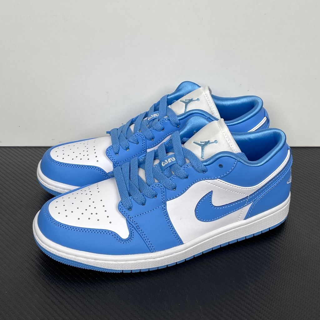 Side profile of the Air Jordan 1 Low sneaker in a classic 'UNC' colorway, featuring a crisp white leather base with vibrant University Blue overlays, a matching Swoosh, and a white midsole resting on a blue rubber outsole.
