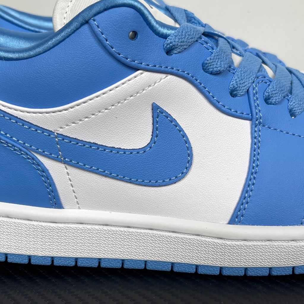 Side profile of the Air Jordan 1 Low sneaker in a classic 'UNC' colorway, featuring a crisp white leather base with vibrant University Blue overlays, a matching Swoosh, and a white midsole resting on a blue rubber outsole.