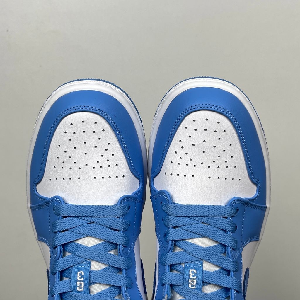 Side profile of the Air Jordan 1 Low sneaker in a classic 'UNC' colorway, featuring a crisp white leather base with vibrant University Blue overlays, a matching Swoosh, and a white midsole resting on a blue rubber outsole.
