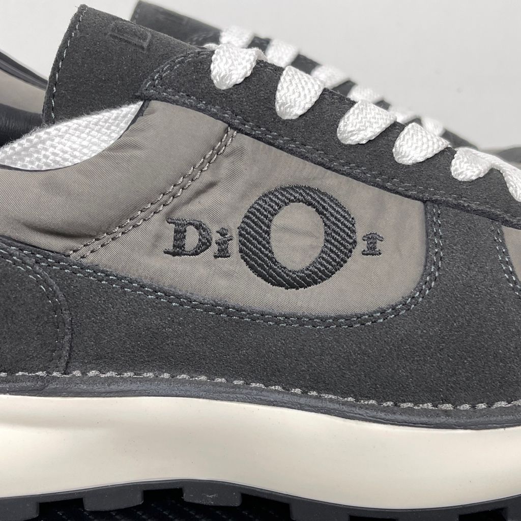Side profile of the Dior Squash sneaker in a black and grey colorway, featuring a mix of premium calf suede and technical nylon, distinctive 'Dior' side embroidery with an oversized 'O', and a chunky white midsole with a lugged black outsole.