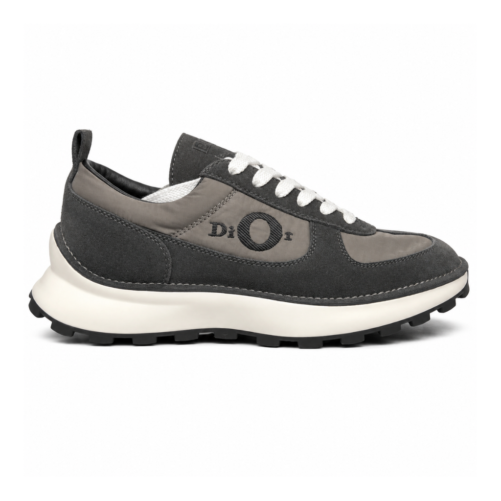 Side profile of the Dior Squash sneaker in a black and grey colorway, featuring a mix of premium calf suede and technical nylon, distinctive 'Dior' side embroidery with an oversized 'O', and a chunky white midsole with a lugged black outsole.