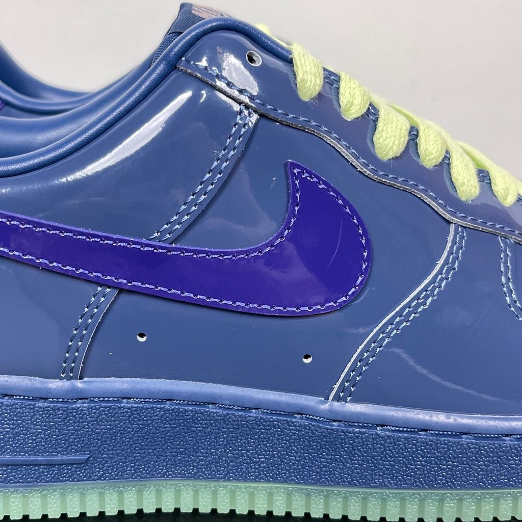 Side profile of the Nike Air Force 1 Low sneaker featuring a high-gloss patent leather upper in deep Mystic Navy, accented by vibrant Grape Ice purple detailing across the Swoosh and branding, resting on a classic white midsole.