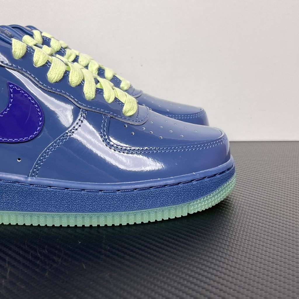 Side profile of the Nike Air Force 1 Low sneaker featuring a high-gloss patent leather upper in deep Mystic Navy, accented by vibrant Grape Ice purple detailing across the Swoosh and branding, resting on a classic white midsole.