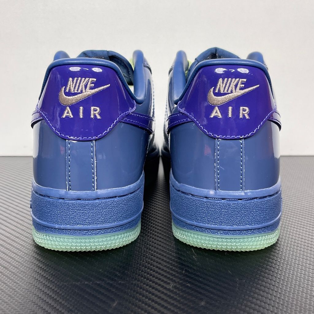 Side profile of the Nike Air Force 1 Low sneaker featuring a high-gloss patent leather upper in deep Mystic Navy, accented by vibrant Grape Ice purple detailing across the Swoosh and branding, resting on a classic white midsole.