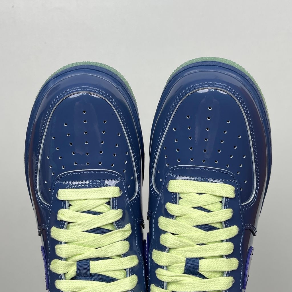 Side profile of the Nike Air Force 1 Low sneaker featuring a high-gloss patent leather upper in deep Mystic Navy, accented by vibrant Grape Ice purple detailing across the Swoosh and branding, resting on a classic white midsole.