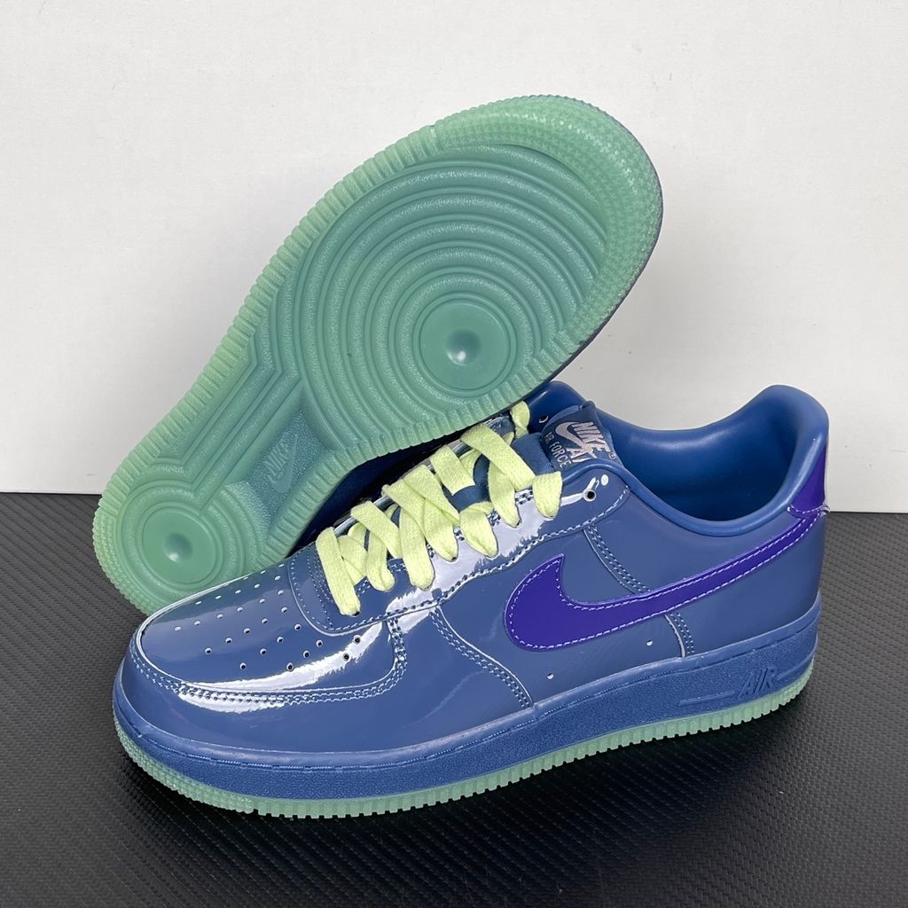 Side profile of the Nike Air Force 1 Low sneaker featuring a high-gloss patent leather upper in deep Mystic Navy, accented by vibrant Grape Ice purple detailing across the Swoosh and branding, resting on a classic white midsole.