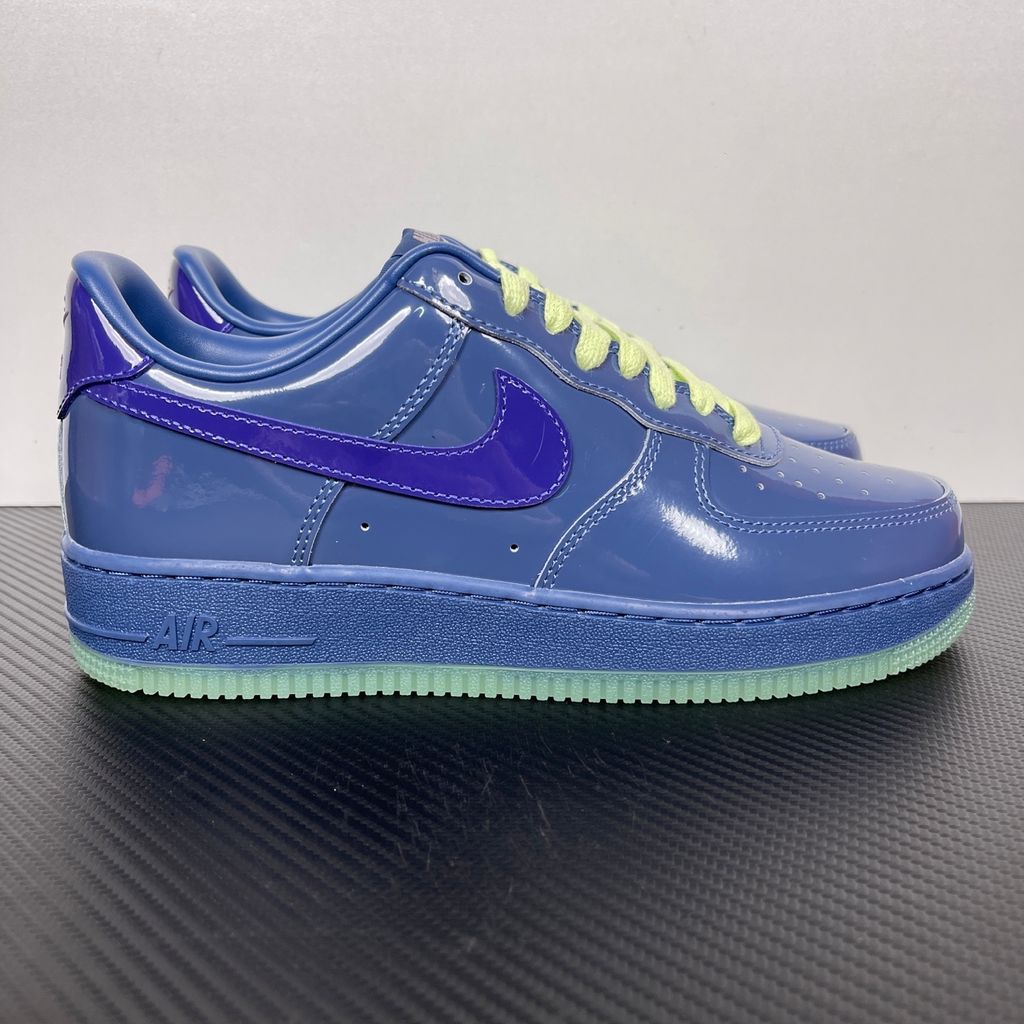 Side profile of the Nike Air Force 1 Low sneaker featuring a high-gloss patent leather upper in deep Mystic Navy, accented by vibrant Grape Ice purple detailing across the Swoosh and branding, resting on a classic white midsole.