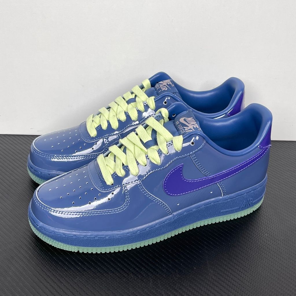 Side profile of the Nike Air Force 1 Low sneaker featuring a high-gloss patent leather upper in deep Mystic Navy, accented by vibrant Grape Ice purple detailing across the Swoosh and branding, resting on a classic white midsole.