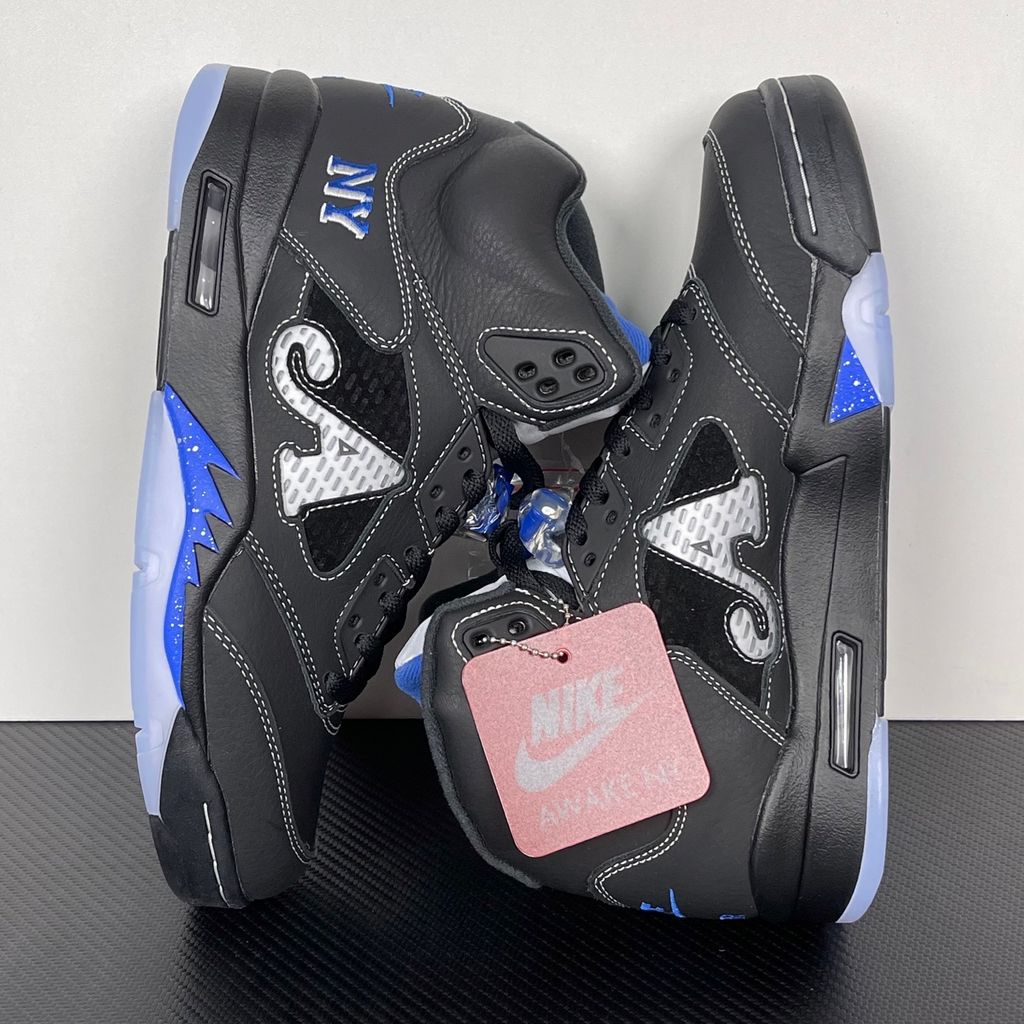 Side profile of the Jordan 5 Retro x Awake NY sneaker in a stealthy black colorway, featuring a premium textured upper, classic translucent midfoot netting, reflective tongue detailing, and signature co-branding on the heel.