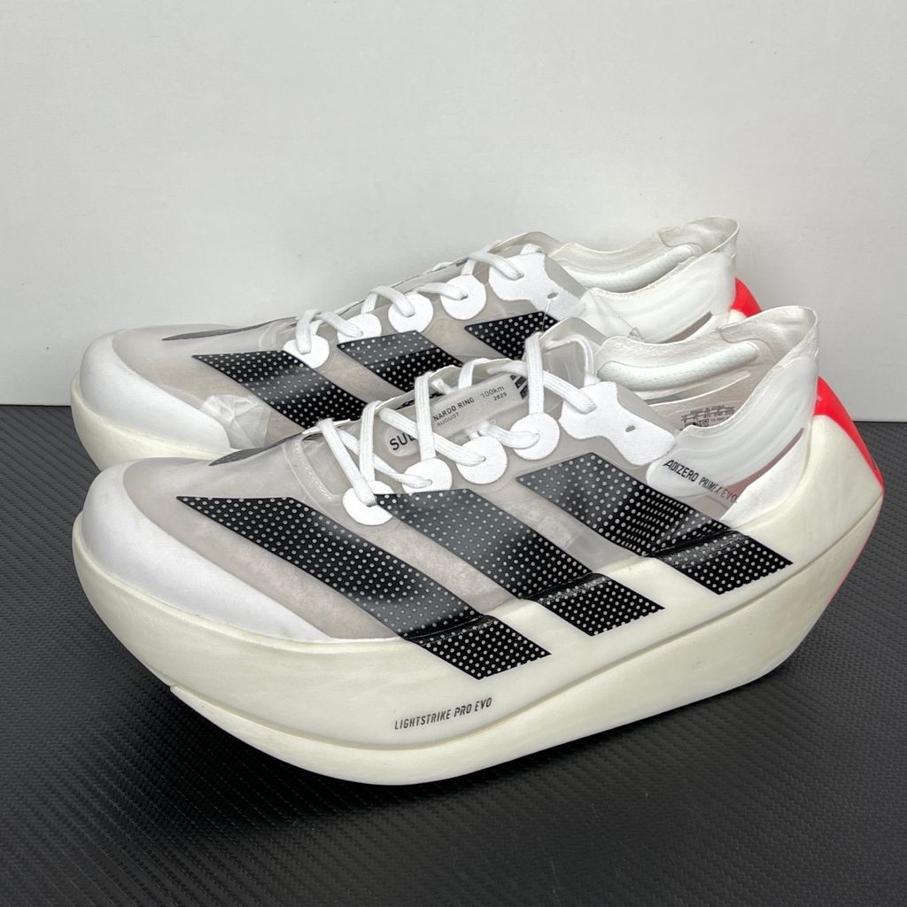 Side profile of the adidas Adizero Prime X EVO running shoe featuring a breathable Cloud White upper, striking Core Black Three Stripes branding, vibrant Lucid Red accents, and a massive, hyper-stacked Lightstrike Pro foam midsole.