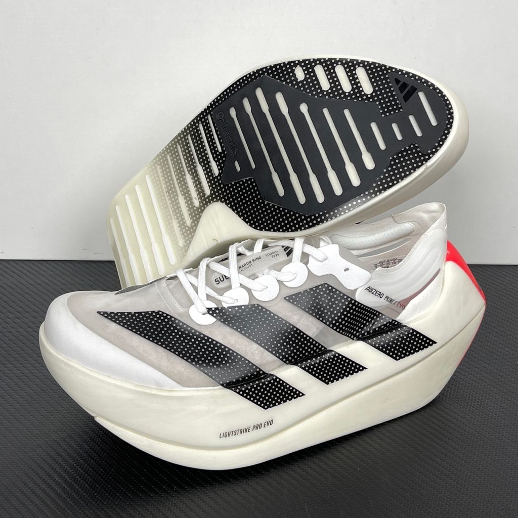 Side profile of the adidas Adizero Prime X EVO running shoe featuring a breathable Cloud White upper, striking Core Black Three Stripes branding, vibrant Lucid Red accents, and a massive, hyper-stacked Lightstrike Pro foam midsole.