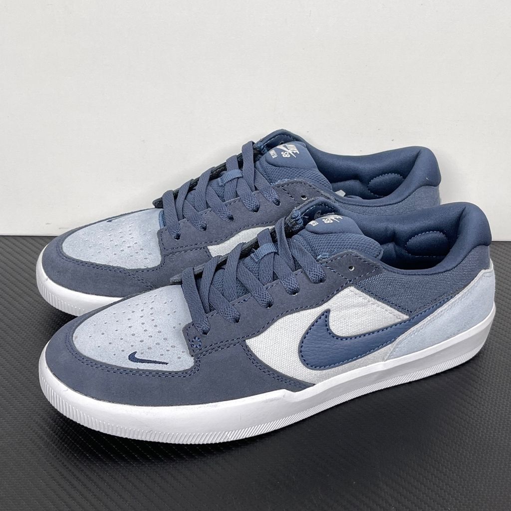 Side profile of the Nike SB Force 58 skate shoe featuring a soft Light Armory Blue canvas and suede upper, accented by a deep Thunder Blue Swoosh and detailing, resting on a crisp white sole with a flexible tri-star tread.