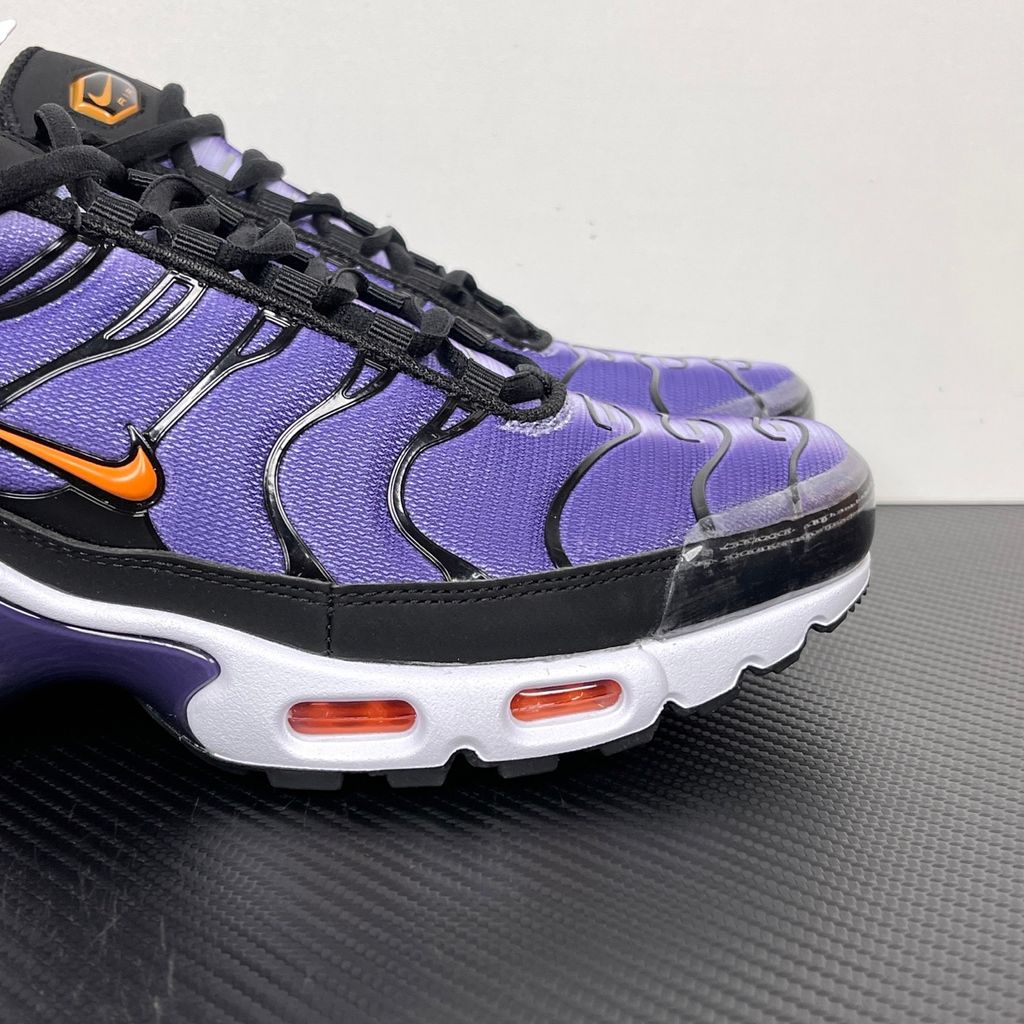 Side profile of the Nike Air Max Plus OG sneaker featuring a vibrant Voltage Purple gradient mesh upper, signature black wavy TPU overlays, striking Total Orange accents on the Swoosh and visible Air units, resting on a crisp white midsole.