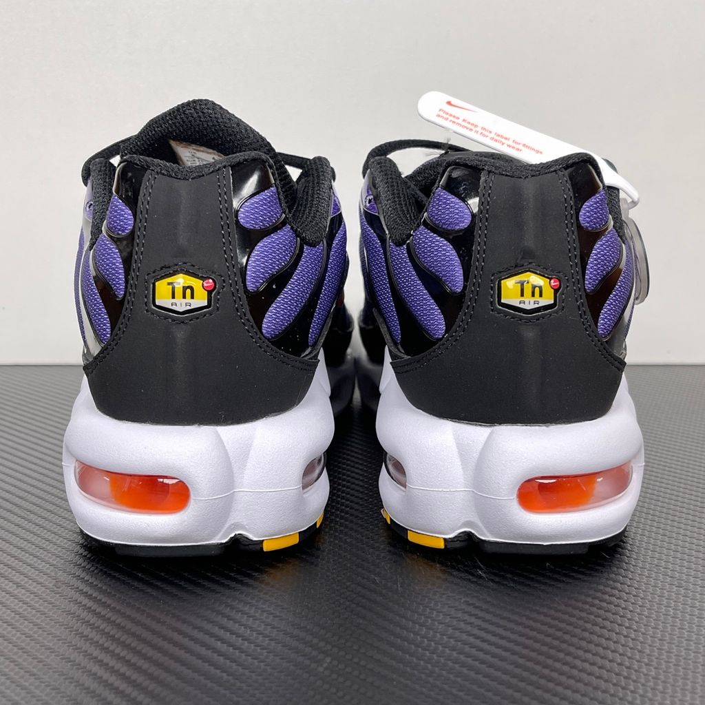 Side profile of the Nike Air Max Plus OG sneaker featuring a vibrant Voltage Purple gradient mesh upper, signature black wavy TPU overlays, striking Total Orange accents on the Swoosh and visible Air units, resting on a crisp white midsole.