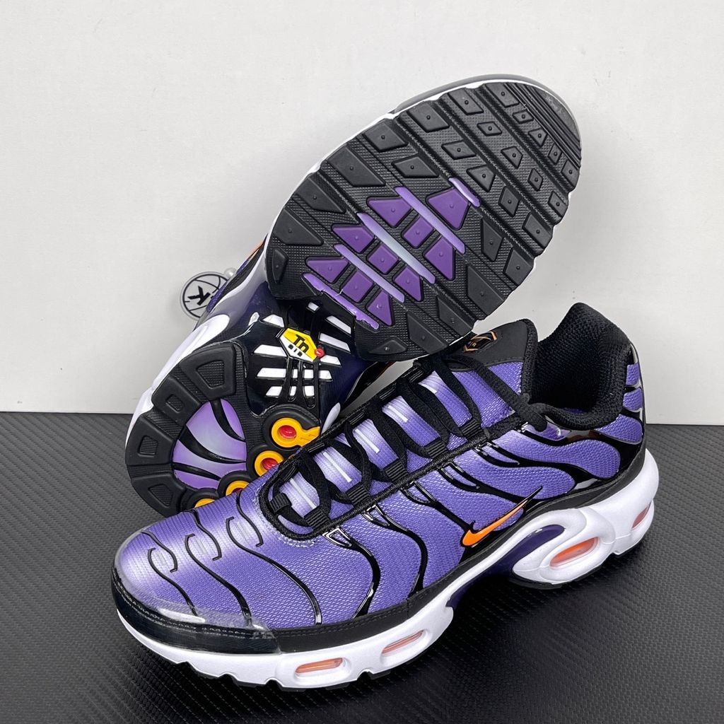 Side profile of the Nike Air Max Plus OG sneaker featuring a vibrant Voltage Purple gradient mesh upper, signature black wavy TPU overlays, striking Total Orange accents on the Swoosh and visible Air units, resting on a crisp white midsole.