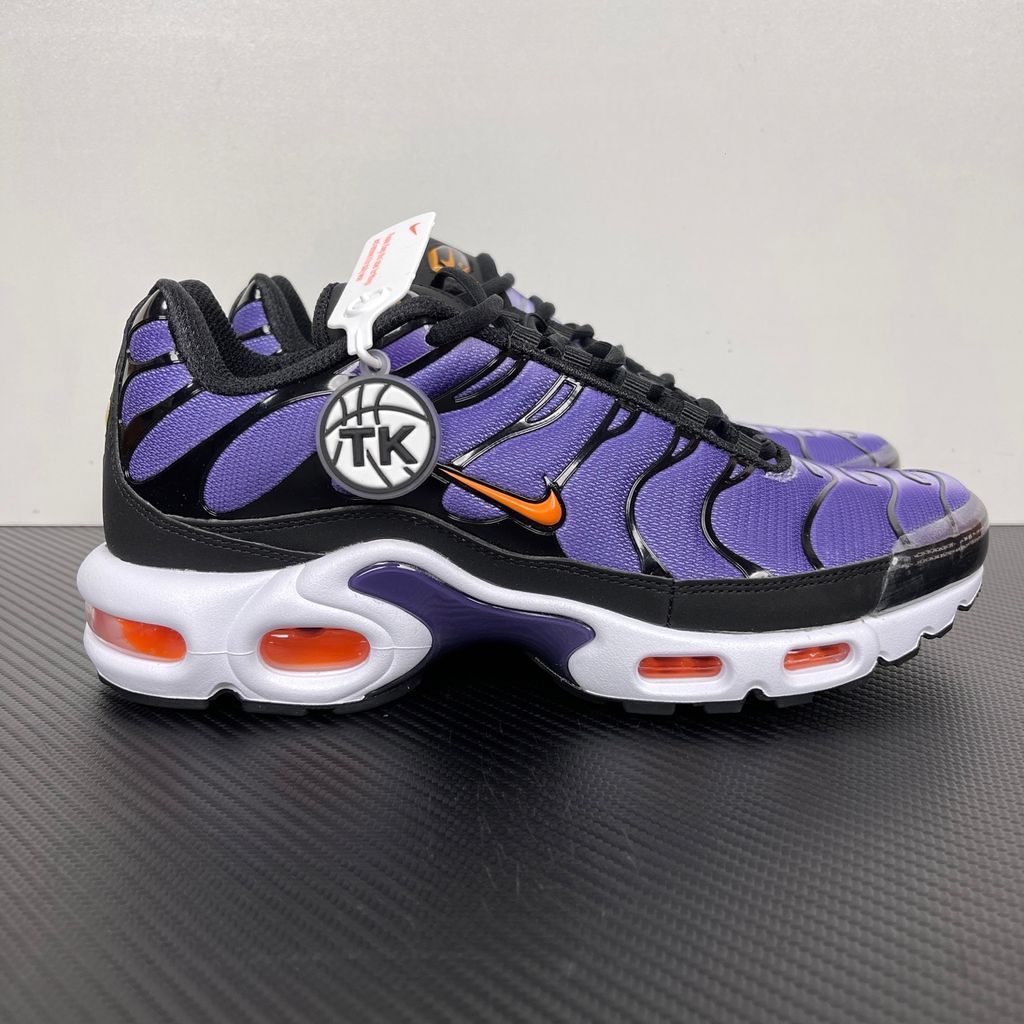 Side profile of the Nike Air Max Plus OG sneaker featuring a vibrant Voltage Purple gradient mesh upper, signature black wavy TPU overlays, striking Total Orange accents on the Swoosh and visible Air units, resting on a crisp white midsole.