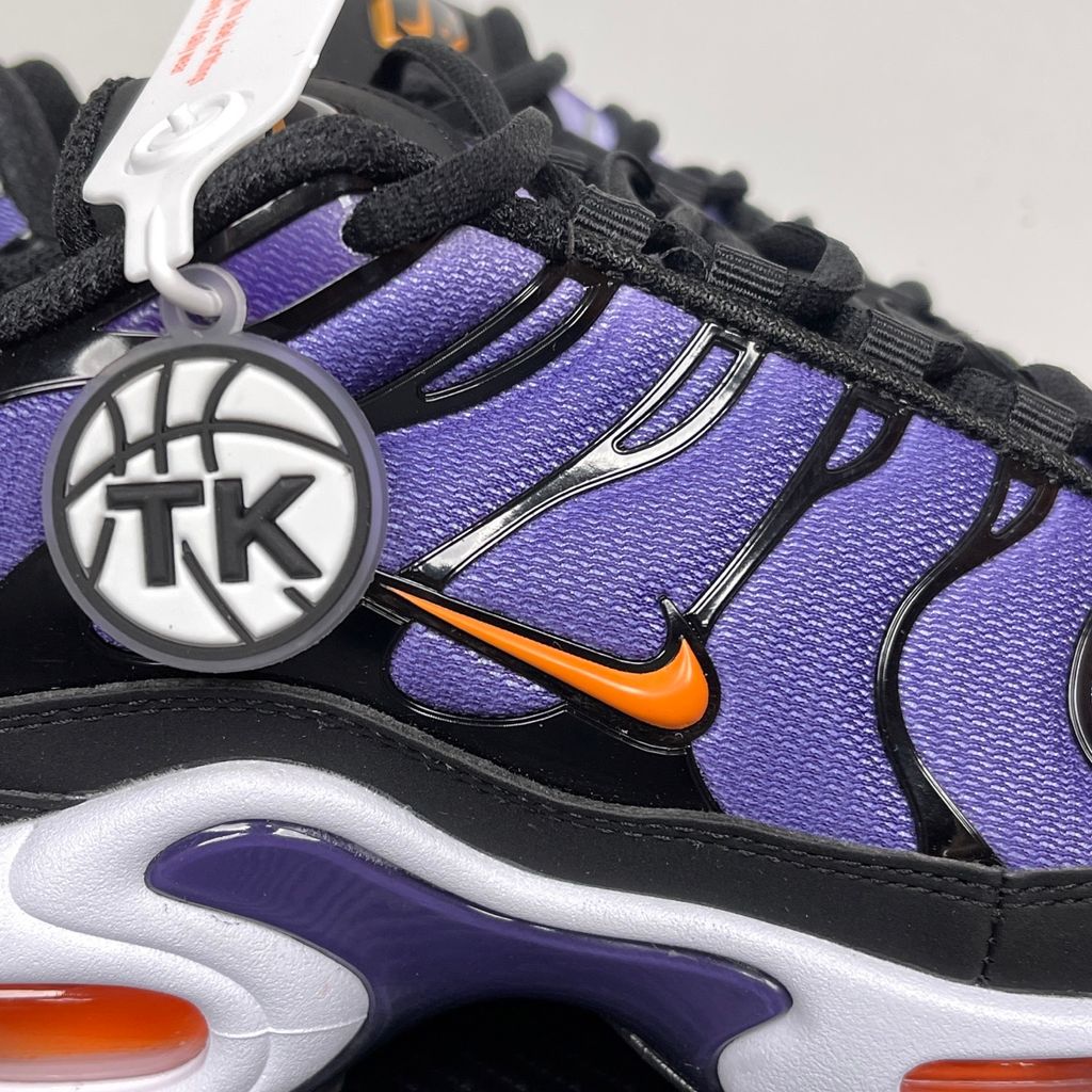 Side profile of the Nike Air Max Plus OG sneaker featuring a vibrant Voltage Purple gradient mesh upper, signature black wavy TPU overlays, striking Total Orange accents on the Swoosh and visible Air units, resting on a crisp white midsole.