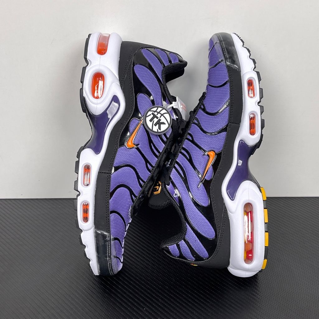 Side profile of the Nike Air Max Plus OG sneaker featuring a vibrant Voltage Purple gradient mesh upper, signature black wavy TPU overlays, striking Total Orange accents on the Swoosh and visible Air units, resting on a crisp white midsole.