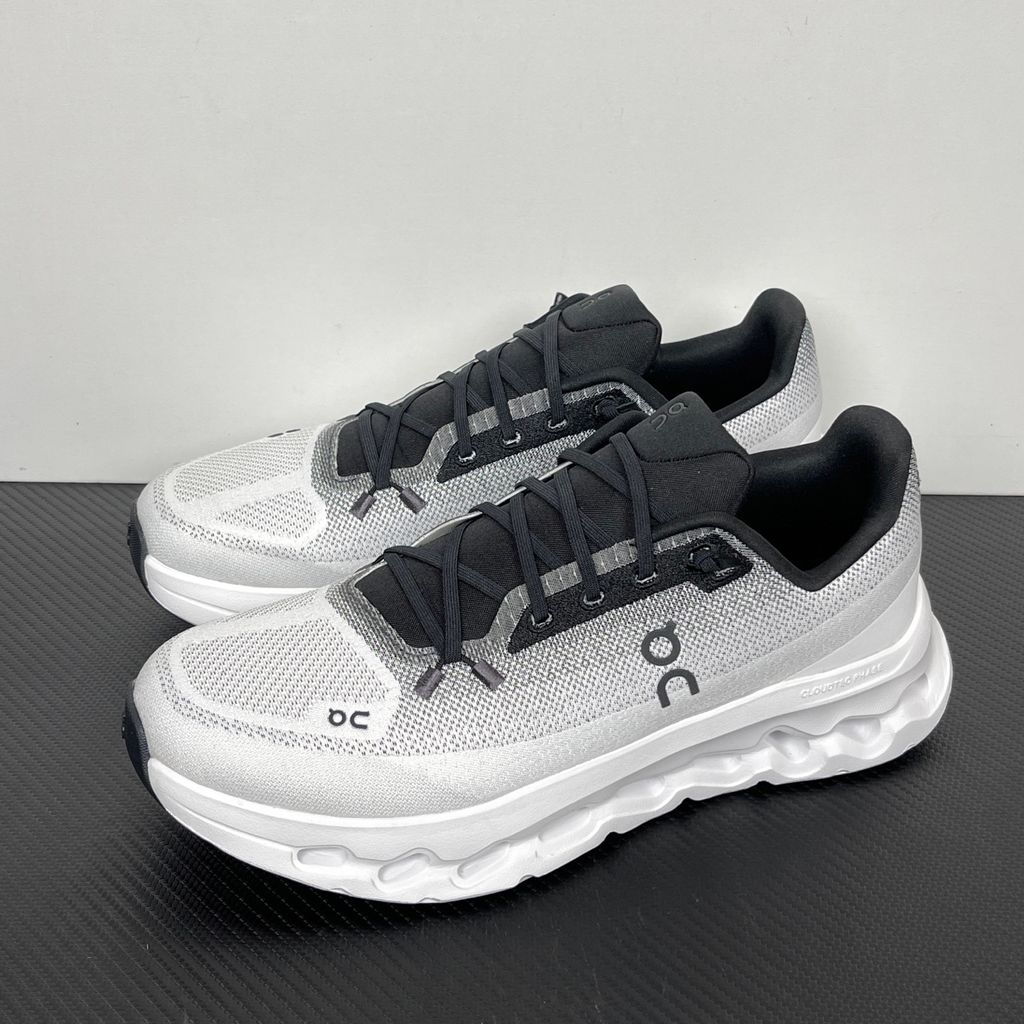 Side profile of the On Running Cloudtilt sneaker featuring a sleek, lightweight black knit upper with a sock-like collar, integrated speed lacing, and a contrasting ivory midsole showcasing the collapsing CloudTec Phase® pods.