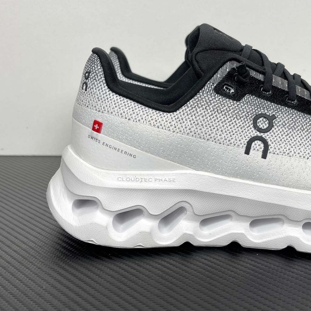 Side profile of the On Running Cloudtilt sneaker featuring a sleek, lightweight black knit upper with a sock-like collar, integrated speed lacing, and a contrasting ivory midsole showcasing the collapsing CloudTec Phase® pods.