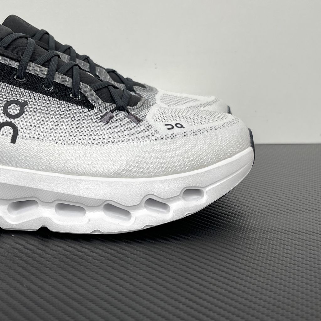 Side profile of the On Running Cloudtilt sneaker featuring a sleek, lightweight black knit upper with a sock-like collar, integrated speed lacing, and a contrasting ivory midsole showcasing the collapsing CloudTec Phase® pods.