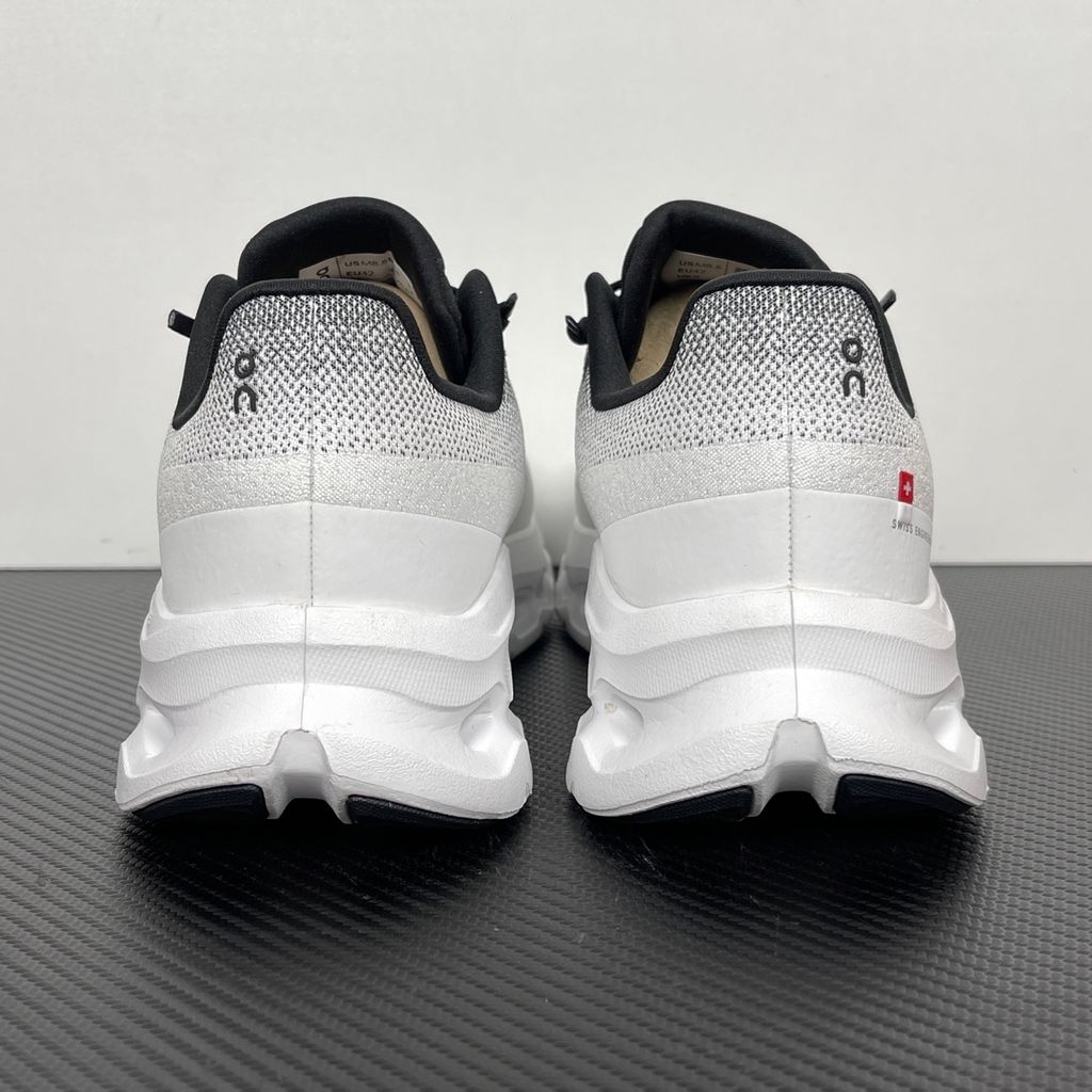 Side profile of the On Running Cloudtilt sneaker featuring a sleek, lightweight black knit upper with a sock-like collar, integrated speed lacing, and a contrasting ivory midsole showcasing the collapsing CloudTec Phase® pods.