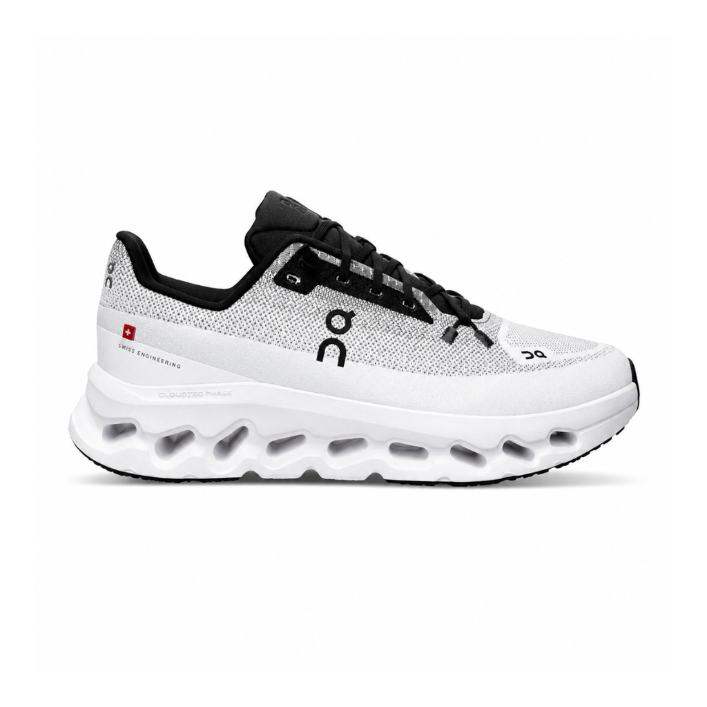 Side profile of the On Running Cloudtilt sneaker featuring a sleek, lightweight black knit upper with a sock-like collar, integrated speed lacing, and a contrasting ivory midsole showcasing the collapsing CloudTec Phase® pods.