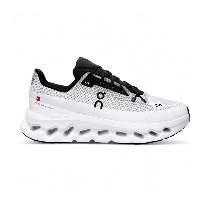 Side profile of the On Running Cloudtilt sneaker featuring a sleek, lightweight black knit upper with a sock-like collar, integrated speed lacing, and a contrasting ivory midsole showcasing the collapsing CloudTec Phase® pods.