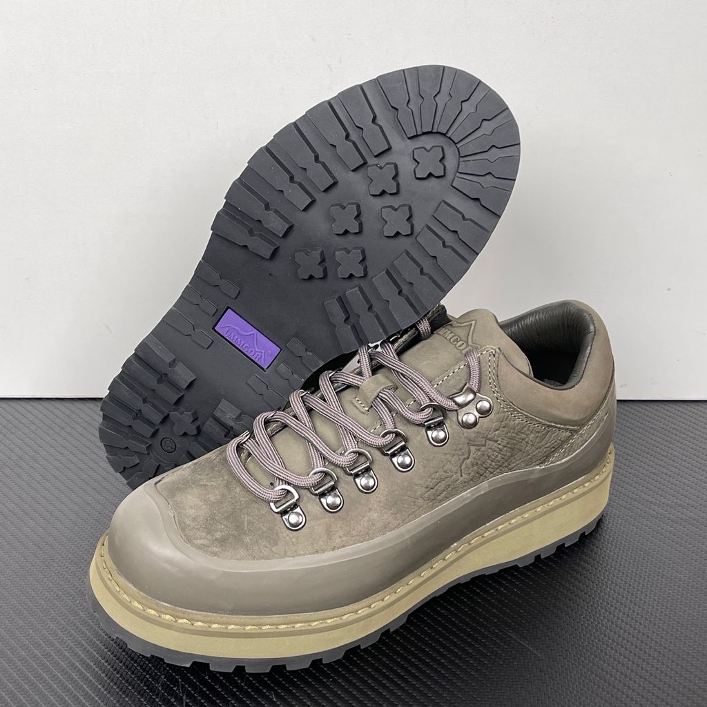 Side profile of the UMMCOR low-top hiking shoe in an earthy Army Green colorway, featuring a textured cowhide leather upper, a protective wrap-around rubber mudguard, metal D-ring lacing hardware, and a chunky lugged rubber outsole.