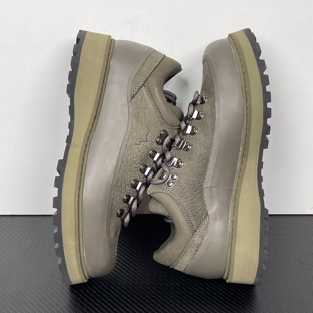 Side profile of the UMMCOR low-top hiking shoe in an earthy Army Green colorway, featuring a textured cowhide leather upper, a protective wrap-around rubber mudguard, metal D-ring lacing hardware, and a chunky lugged rubber outsole.